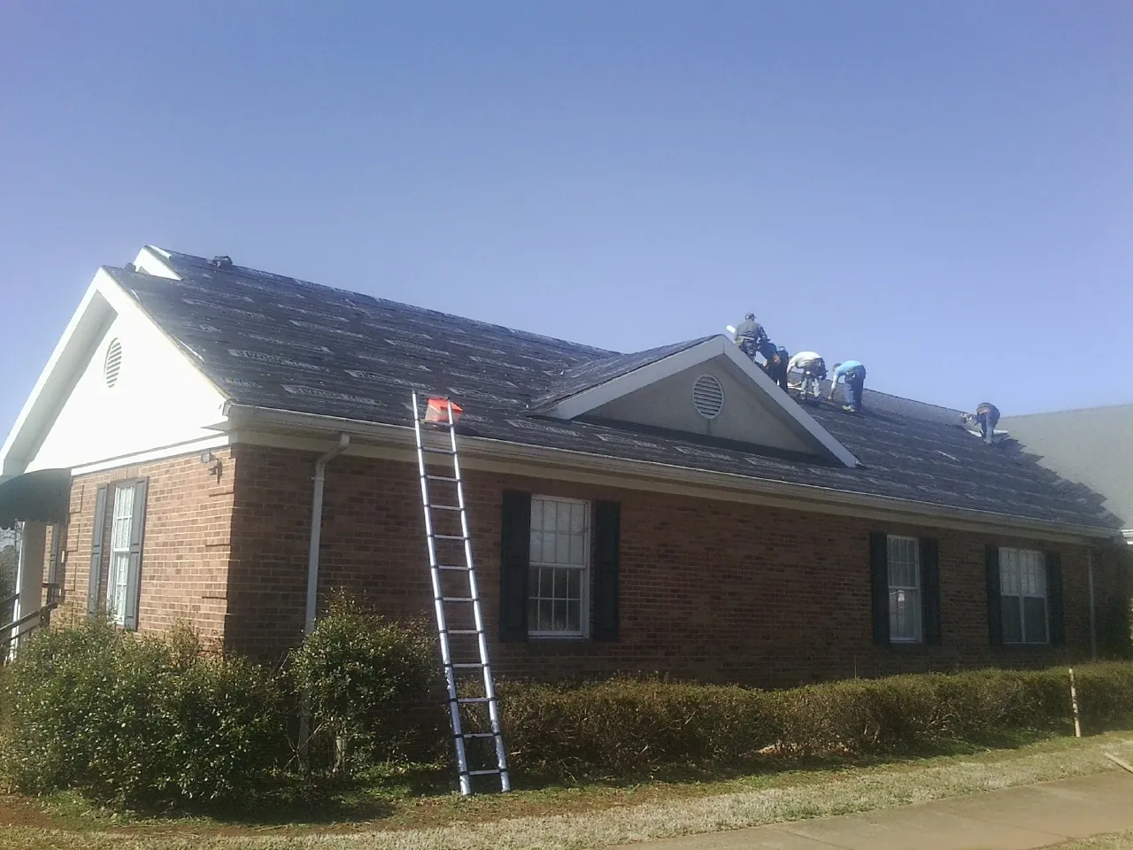 Crew tearing shingles off a brick ranch roof with a ladder set — Emergency Roof Repair work by our crew in Trail