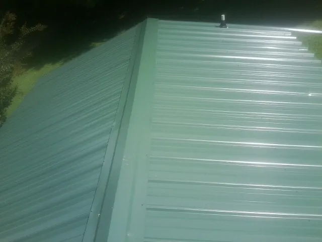 New green metal panels meeting at the ridge of a roof — Flat Roof Repair work by our crew in Trail